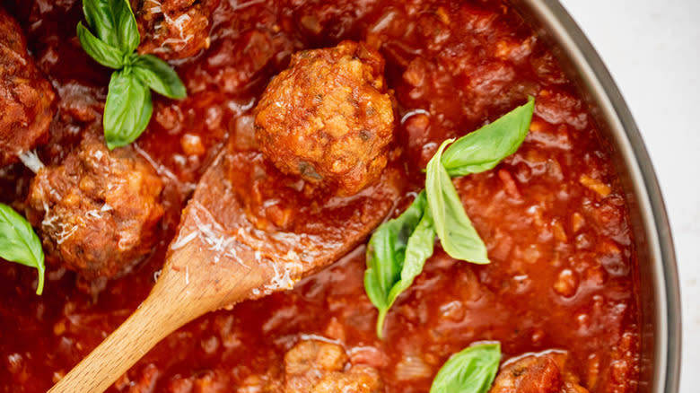 Spooning meatball from pan of tomato sauce with fresh basil