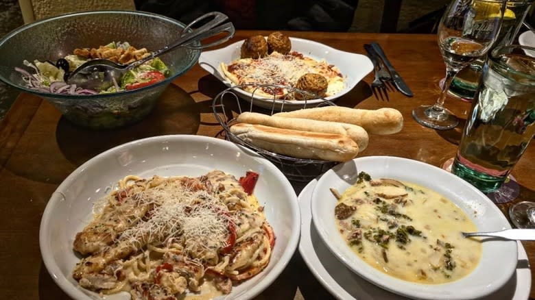 Soup, salad, breadsticks, and two plates of pasta on Olive Garden table.