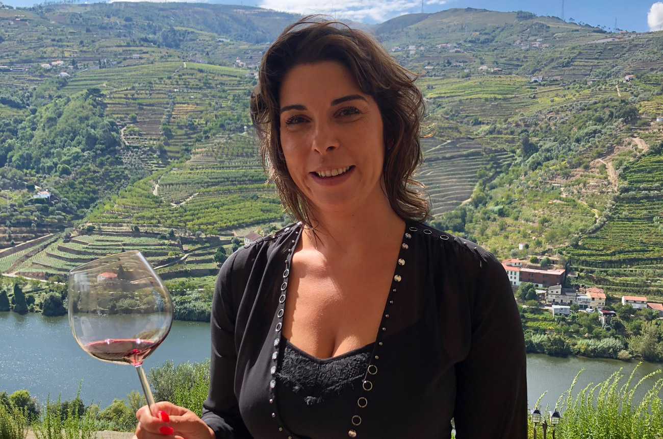 A woman standing with a glass of wine with valley vineyards behind