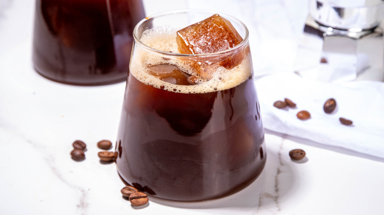 A cocktail glass filled with a dark brown liquid on a marble countertop with espresso beans scattered around the glass.