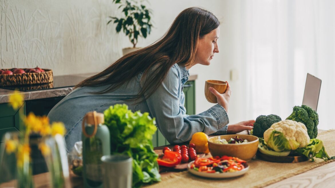 woman looks at laptop while surrounded by healthy foods in her kitchen
