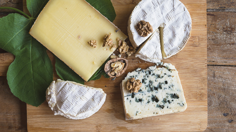Assorted cheeses on a board with walnuts and fig leaves