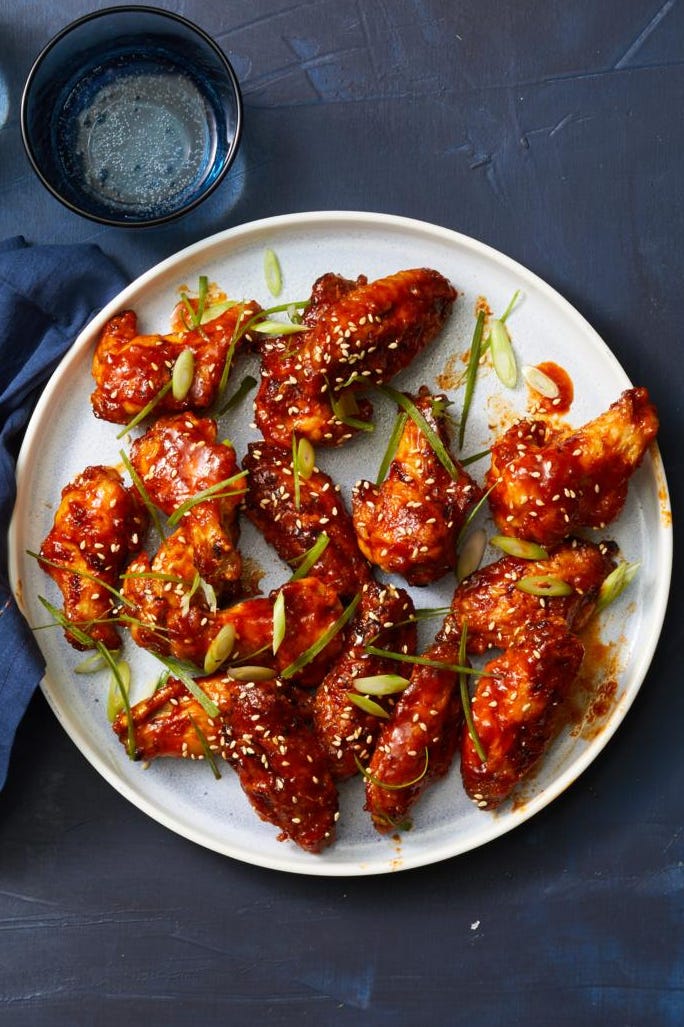 plate of glazed chicken wings garnished with sliced green onions and sesame seeds accompanied by two blue glasses