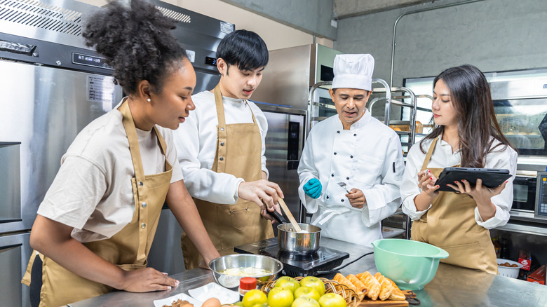 A group of three young students working with a chef in a professional kitchen.