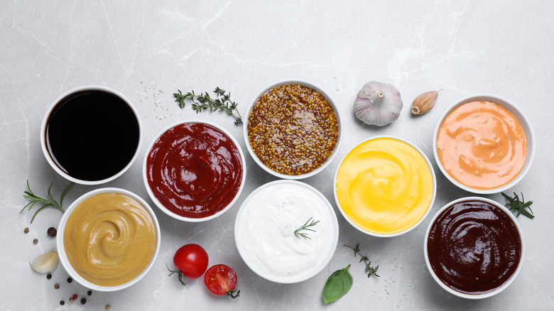 A variety of sauces, mustards, and condiments in ramekins on a gray countertop