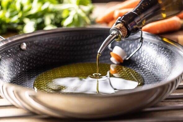 Olive oil is poured from a bottle into a modern non-stick frying pan. Healthy eating and cooking concept