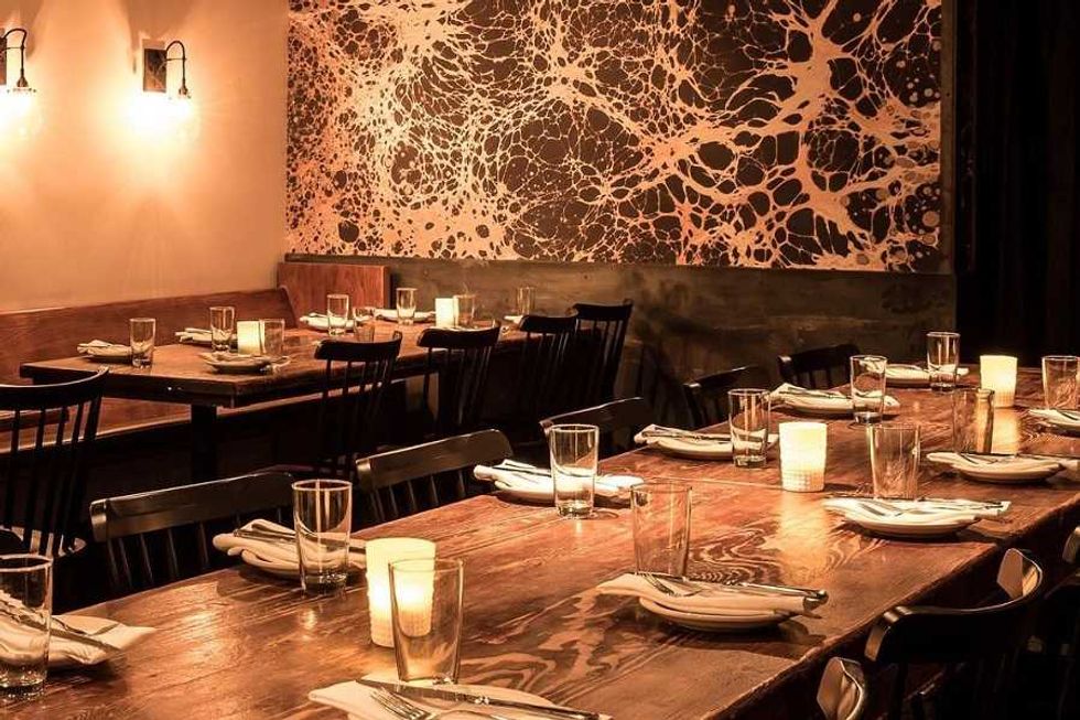 Cozy restaurant with wooden tables, black chairs, candles, and abstract wall art.