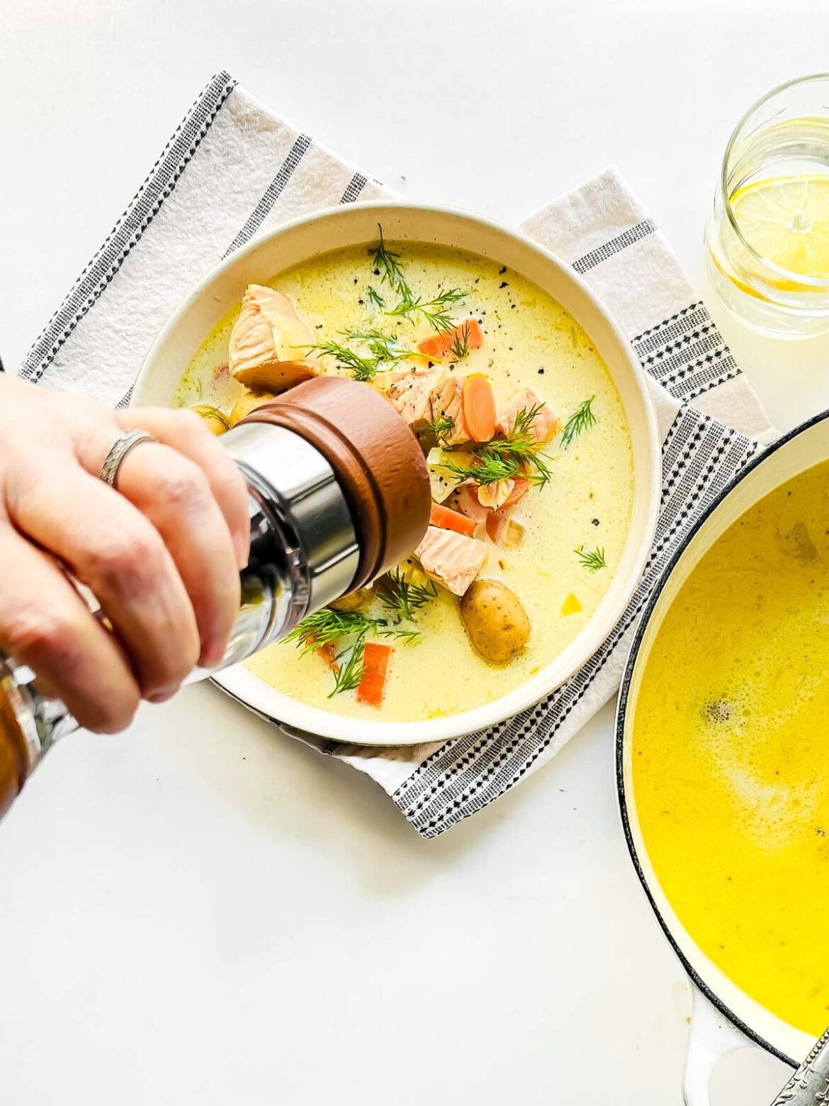 Adding fresh cracked black pepper to creamy lemon salmon soup.
