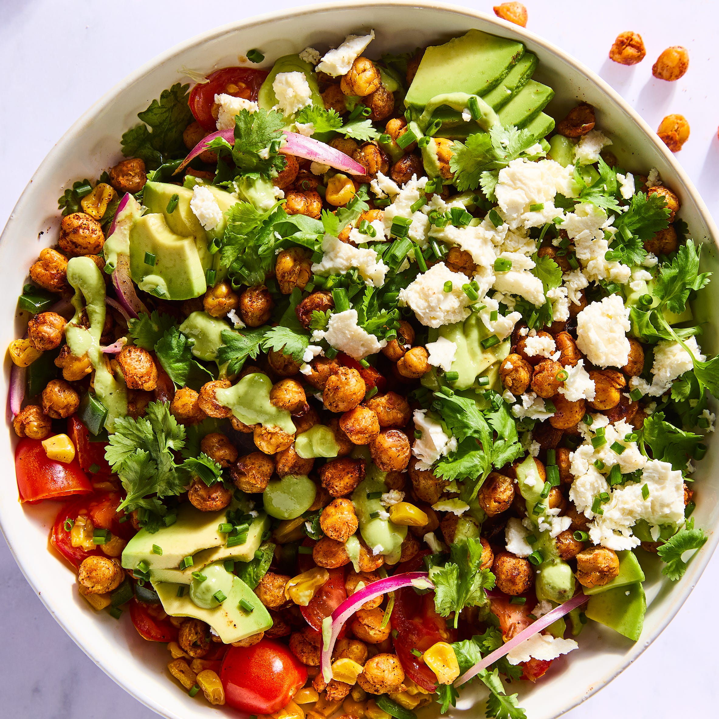 salad tossed with crispy chickpeas, avocado slices, red onions, sliced tomatoes, corn, and topped with herbs and cheese