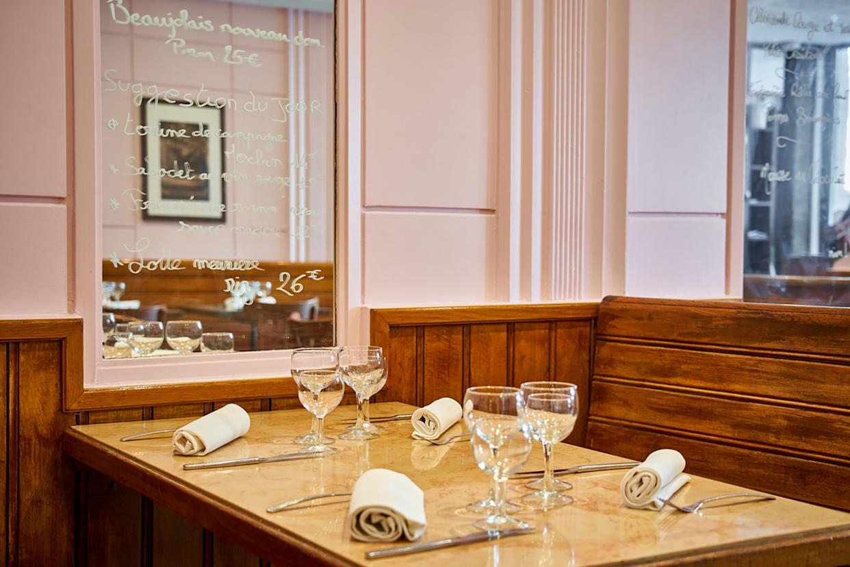 A charming and clean restaurant booth, decked with linen napkins and wine glasses next to a wall mirror with the menu written on it.