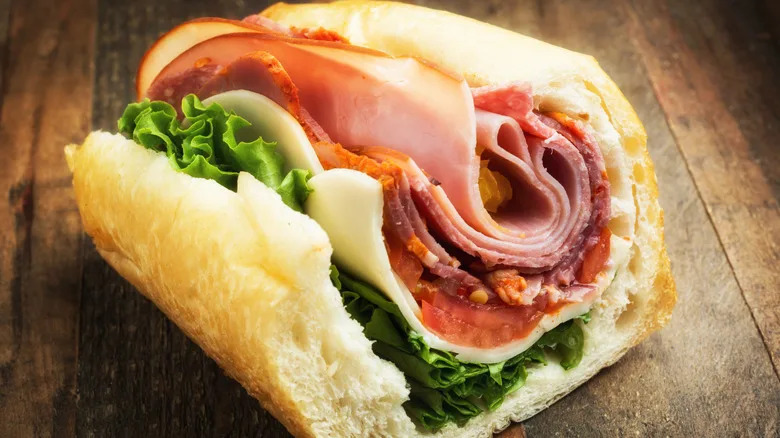 Ham, mortadella, salami, pepperoncini, provolone, tomato and lettuce are layeres in a baguette bun