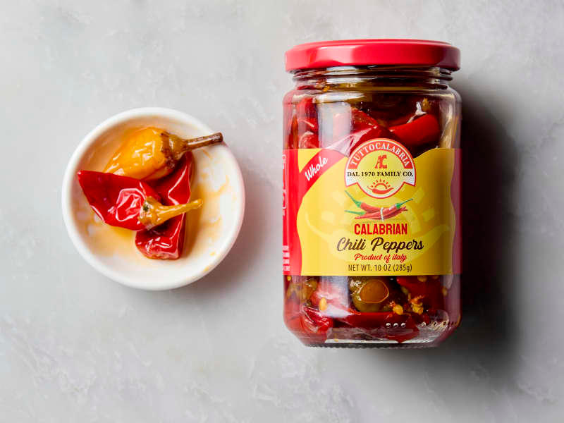 overhead shot of a small white bowl with three calabrian chilis, and the jar to the right of it.
