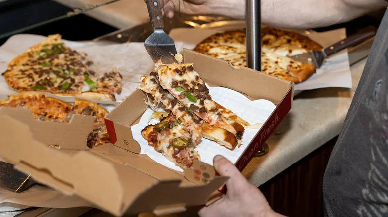 A person feeling a chico box with slices of pizza from several different pizzas