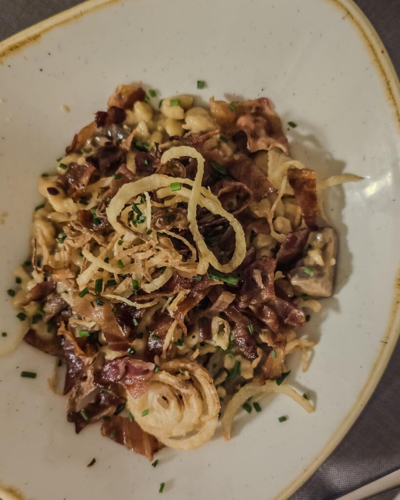 Dinner in Tessin, Switzerland. Spätzli with mushrooms and bacon, bao with brasato and coleslaw, cabbage leaves filled with potato and emmenthaler with cheese fondue and fried onions, brasato with polenta, cod fish with tomatoes and olives, apple cake