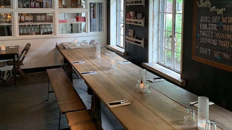 A long wooden table next to white shelving and a black chalkboard in Saraghina Restaurant