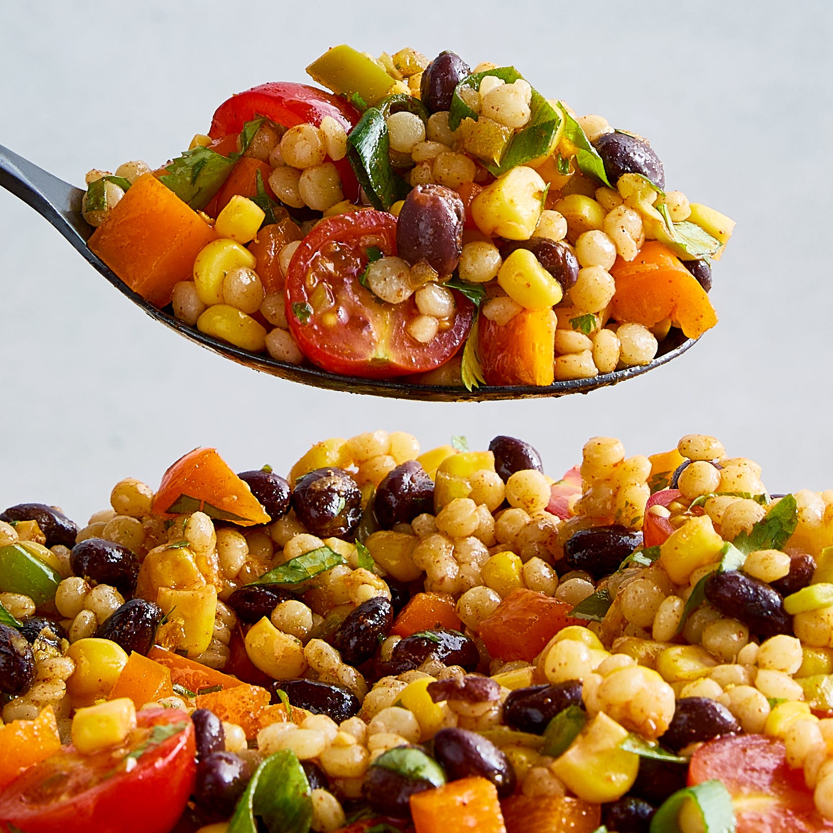 a bowl with pearl couscous, black beans, corn, bell peppers, cherry tomatoes, scallions, cilantro, and pickled jalapenos