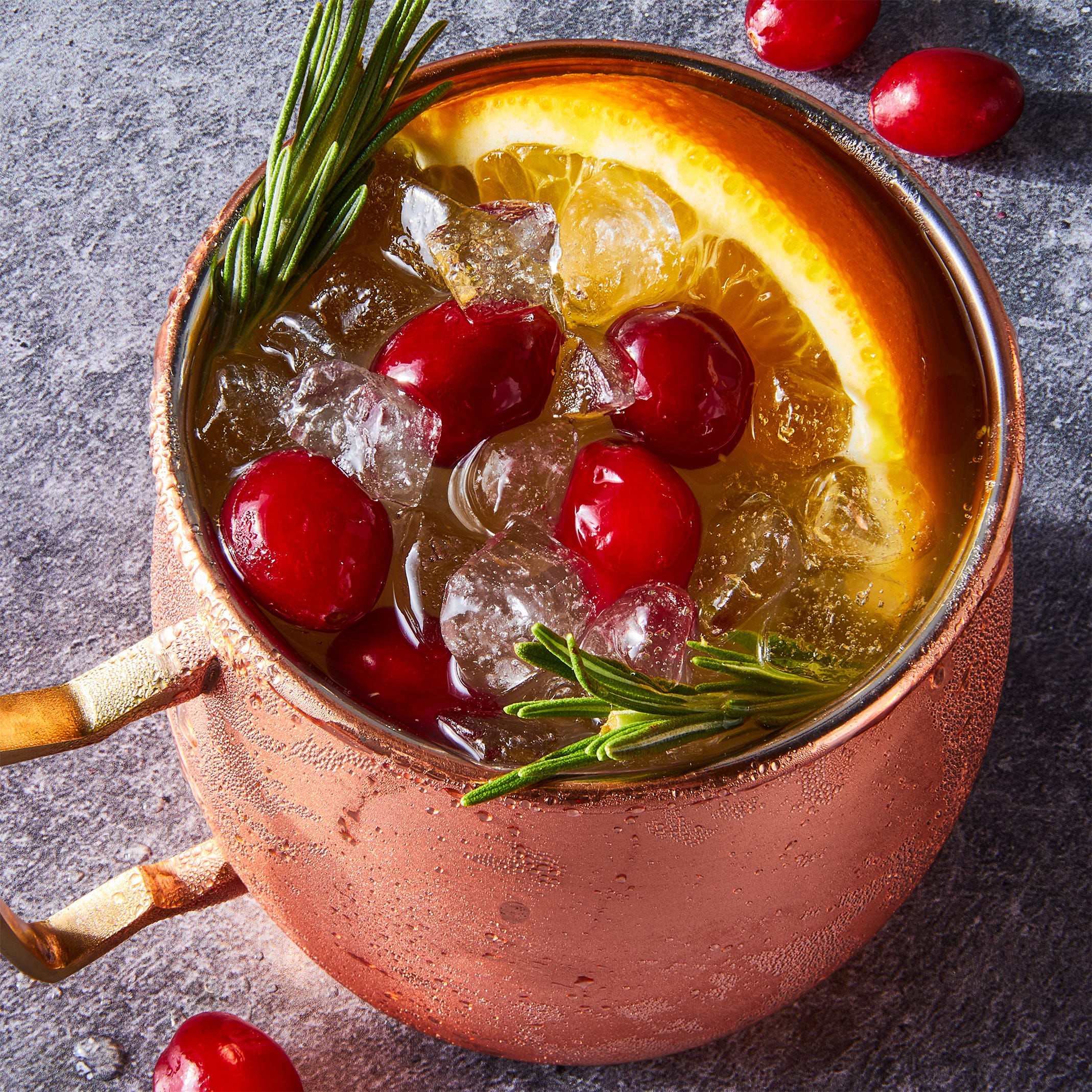cranberry orange mule served in copper mugs and garnished with fresh cranberries, orange slices, and rosemary sprigs