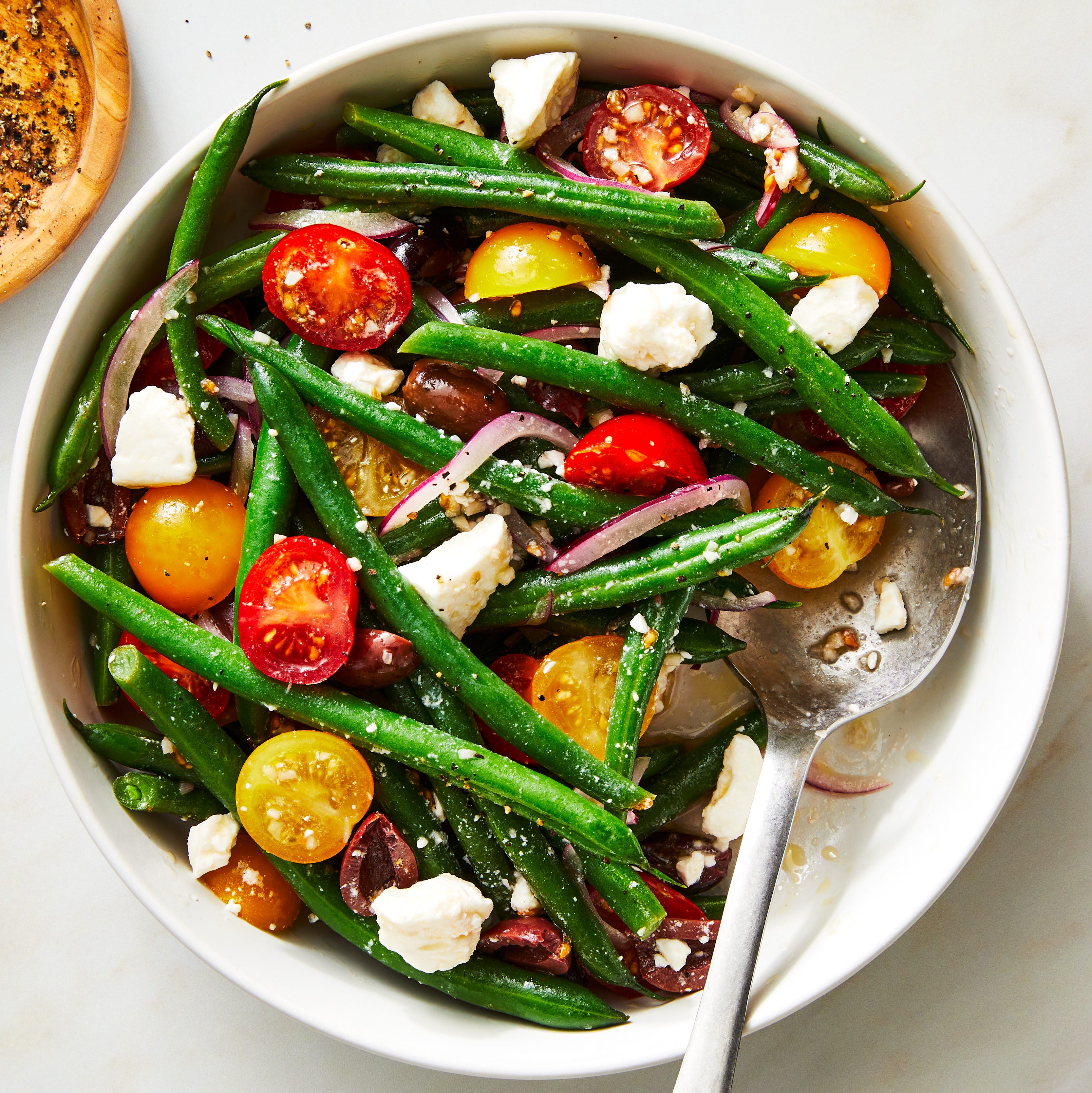 green bean salad with tomatoes and feta in a bowl with a spoon