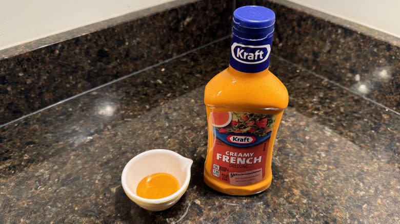 Kraft dressing on a countertop next to small white dish containing dressing