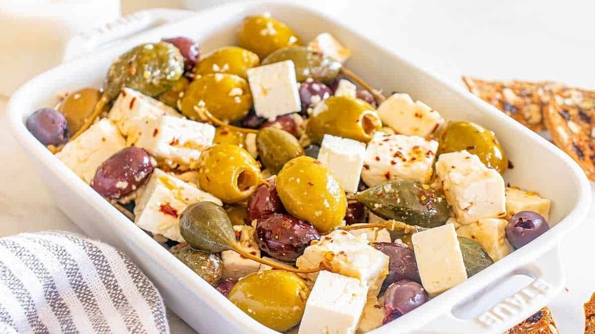 A white ceramic oven tray filled with Marinated Olives with Feta.