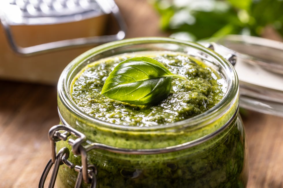Close-up view of a glass full of fresh green basil pesto with a leaf on top.
