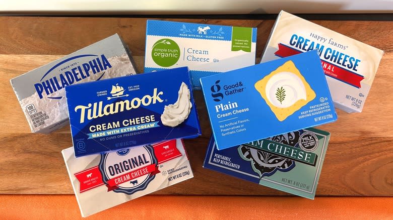 7 brands of brick cream cheese stacked like a pyramid on black counter with white backdrop