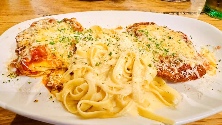 White plate of fettuccine Alfredo next to lasagna and chicken Parmigiana from Olive Garden