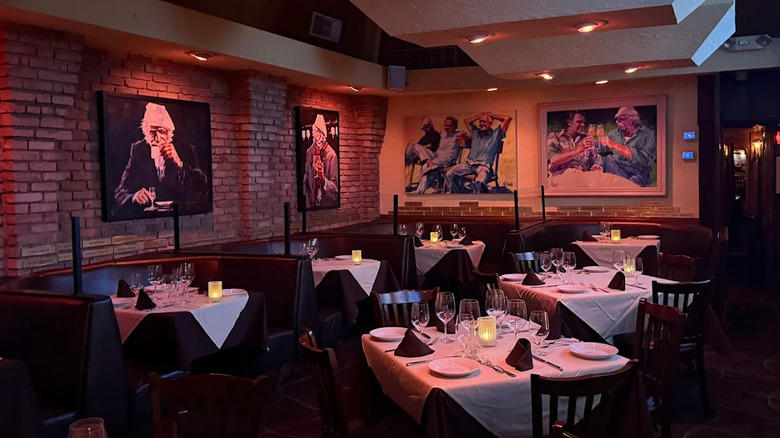 Interior view of Piero's Italian Cuisine in Las Vegas, with exposed brick wall, artwork on the wall of various celebrities drinking, and dark wood tables and booths with dim lighting