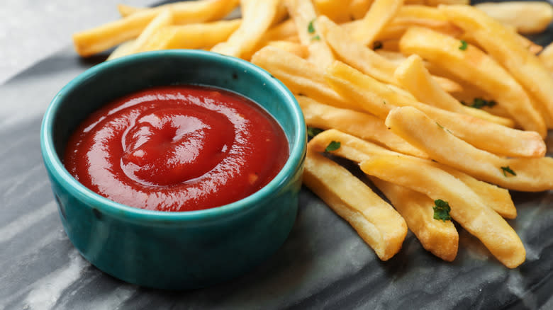 French fries with ketchup in a small blue ceramic cup.