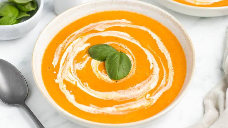 Bowl of tomato soup topped with cream and fresh basil leaves
