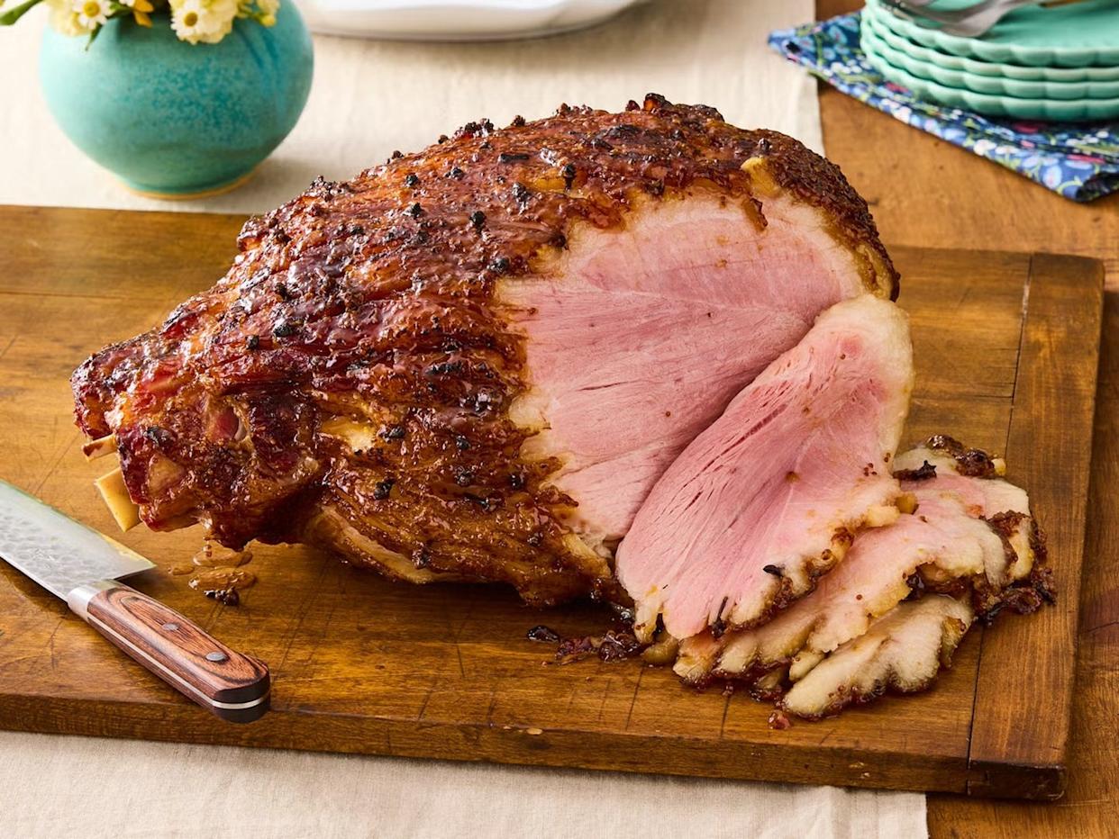 Sliced glazed ham on a wooden cutting board with a knife.