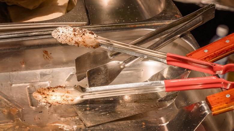 Dirty tongs and food trays that need to be cleaned