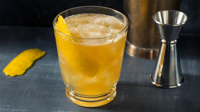 A golden hued cocktail with a twist of lemon on a gray countertop.