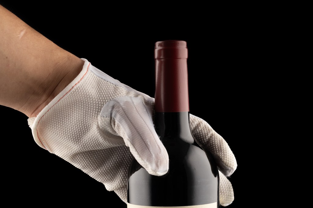 Hand, wearing a white glove, holding a bottle of red wine.