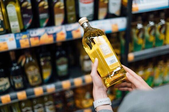 Close up of young woman grocery shopping in a supermarket. Standing by the aisle, holding a bottle of organic cooking oil, readi