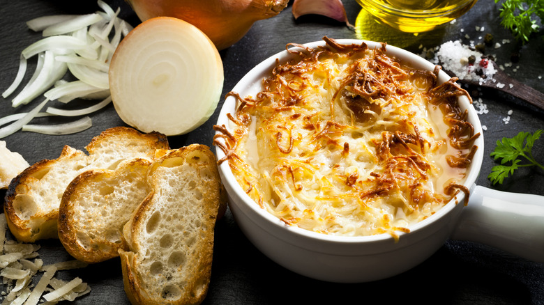 A bowl of French onion surrounded by raw onions and bread