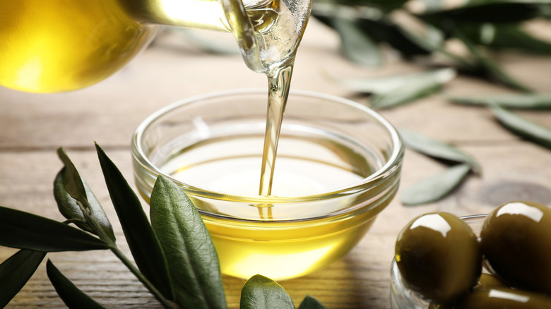 Pouring olive oil into a small bowl with green olives and olive branches