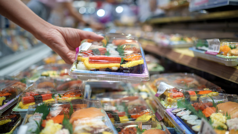 Someone grabbing a tray of grocery store sushi out of the cooler