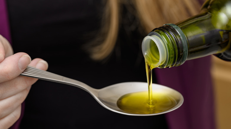 A woman pouring oil into a spoon.