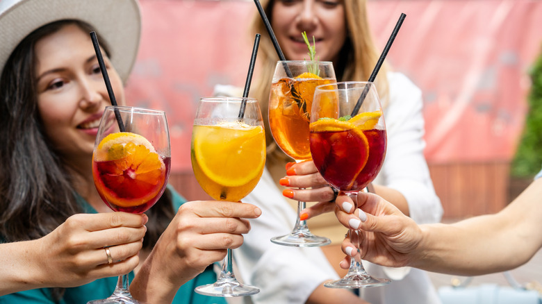 Four friends cheers tropical drinks in wine glasses.