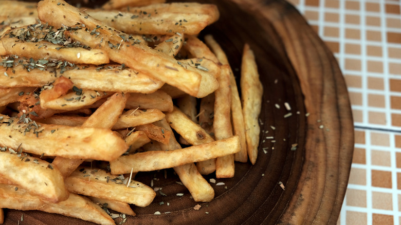 French fries on a wooden plate seasoned with herbs.