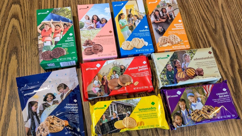 Nine colorful boxes of various Girl Scout cookies on a wood table