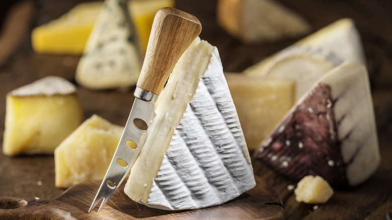 Assorted wedges of cheese on a wooden cheese board with a cheese knife
