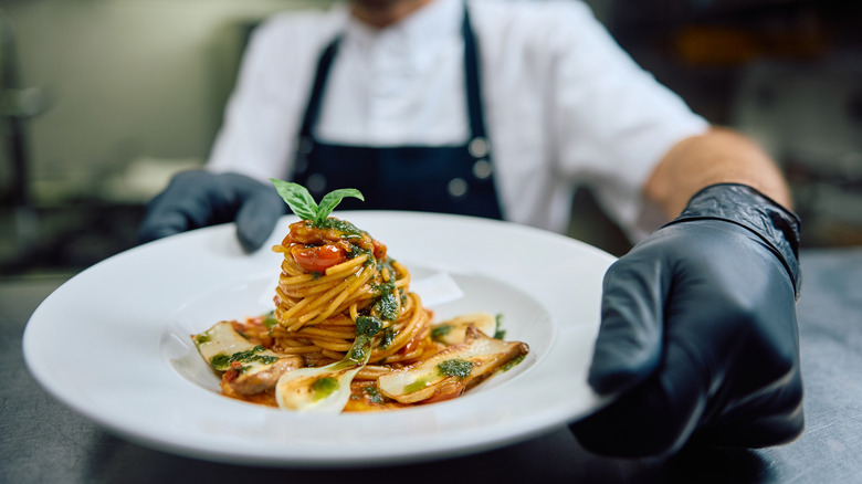 A chef puts a pasta dish up on the counter at a restaurant.