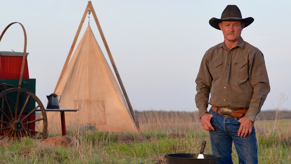 Kent Rollins stands next to a cast-iron grill and a tent.