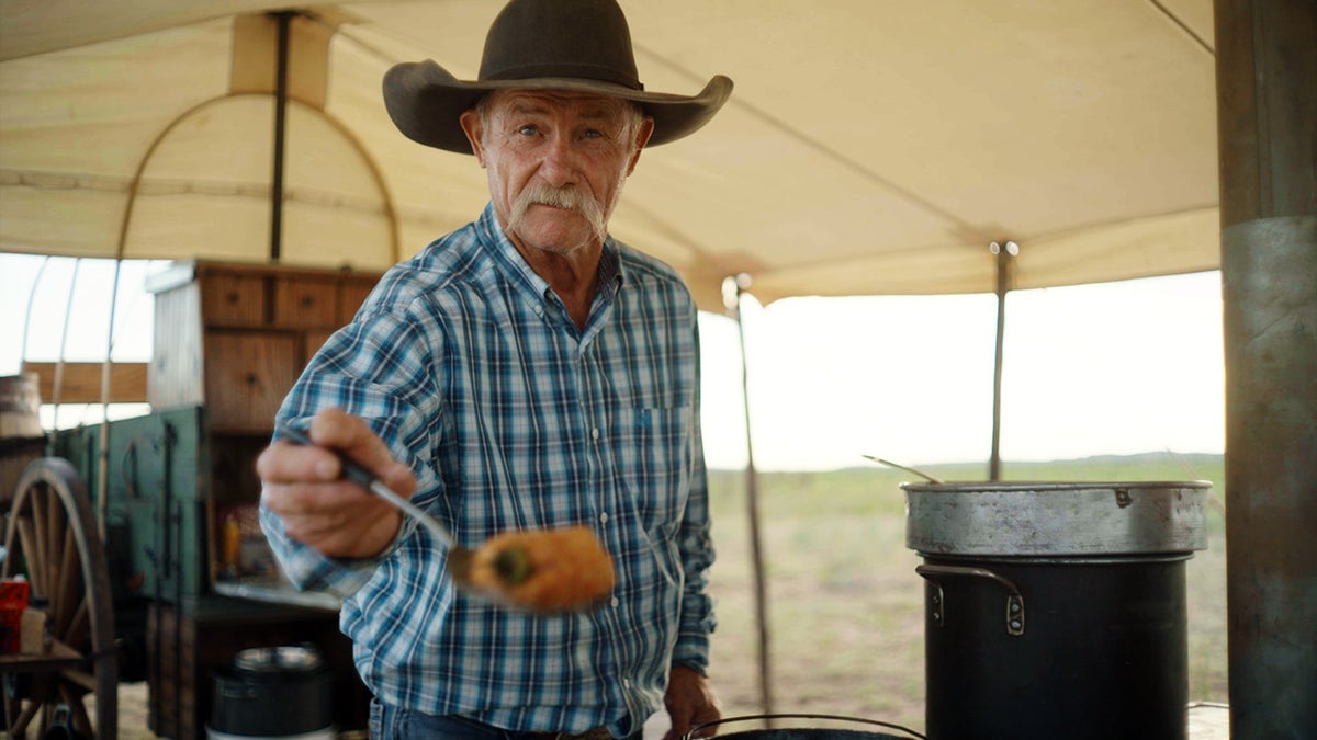 Cowboy chef Kent Rollins holds spoonfull of stew at campsite.