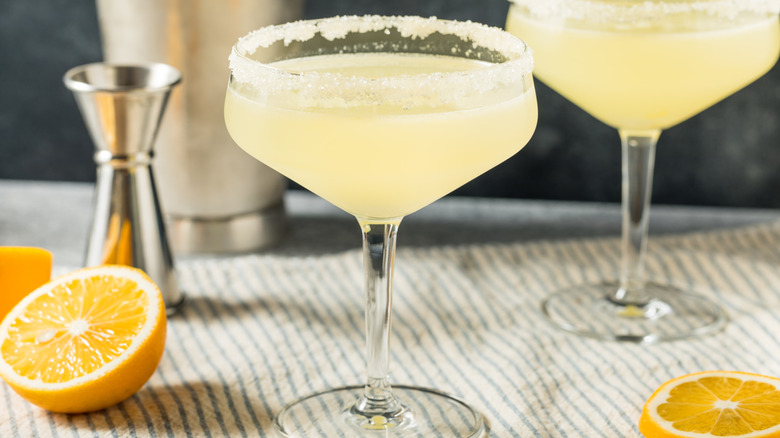 Pale yellow cocktail in a martini glass with a sugared rim next to half of a lemon.