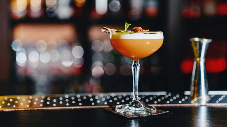 A refreshing orange-colored cocktail in a coupe glass on a wooden bar.