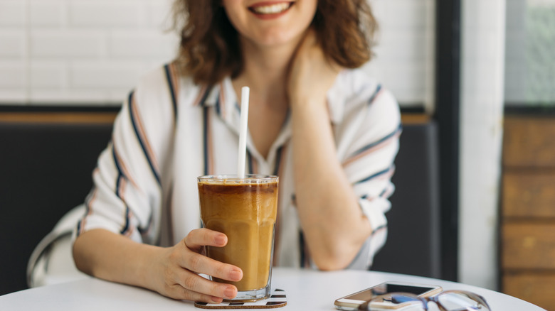 Woman smiling as she holds glass of iced coffee