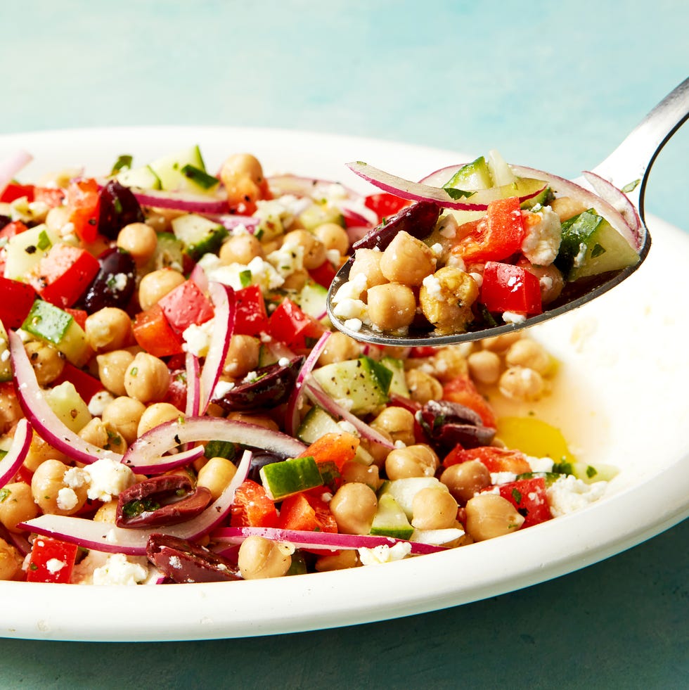 chickpeas with olives, feta, cucumbers, sliced red onion, and red bell peppers on a white platter